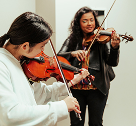 A girl standing playing violin with violin teacher