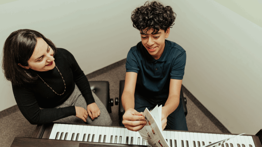 Teen student smiling while learning piano with a teacher during a music lesson at The Piano Studio.