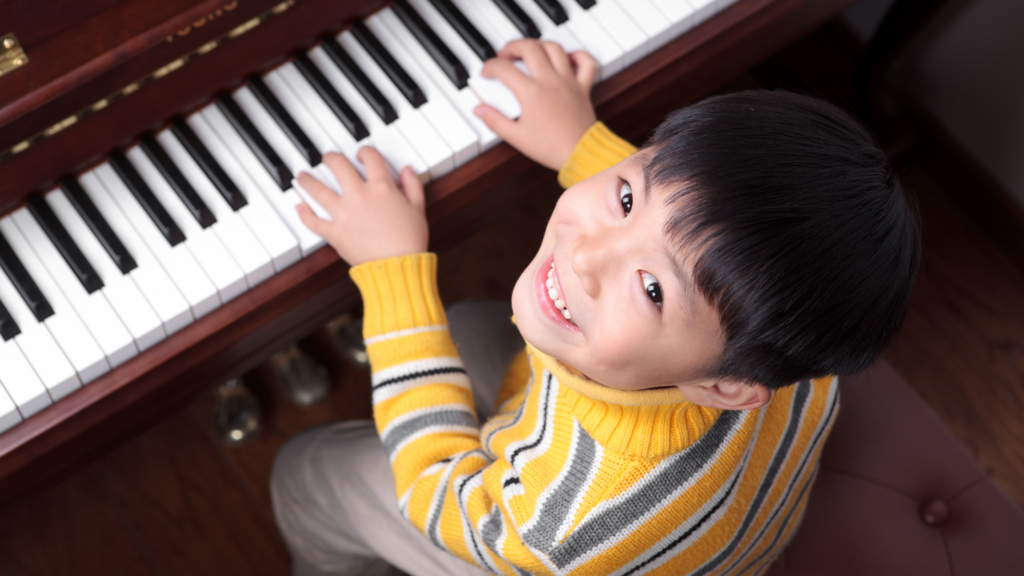 Young boy smiling while playing the piano during a music lesson.