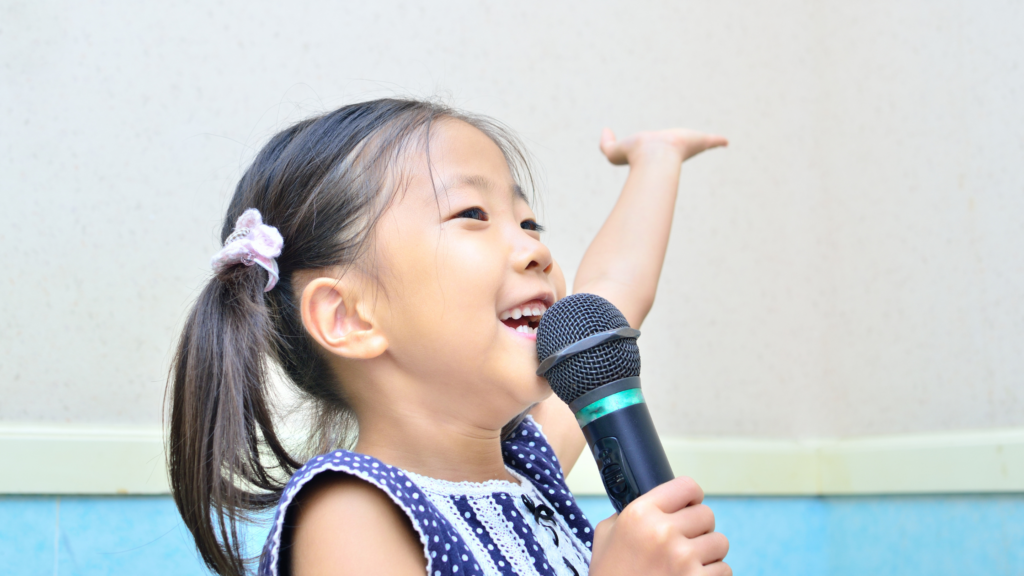 Happy young girl singing into a microphone during a children’s voice lesson.