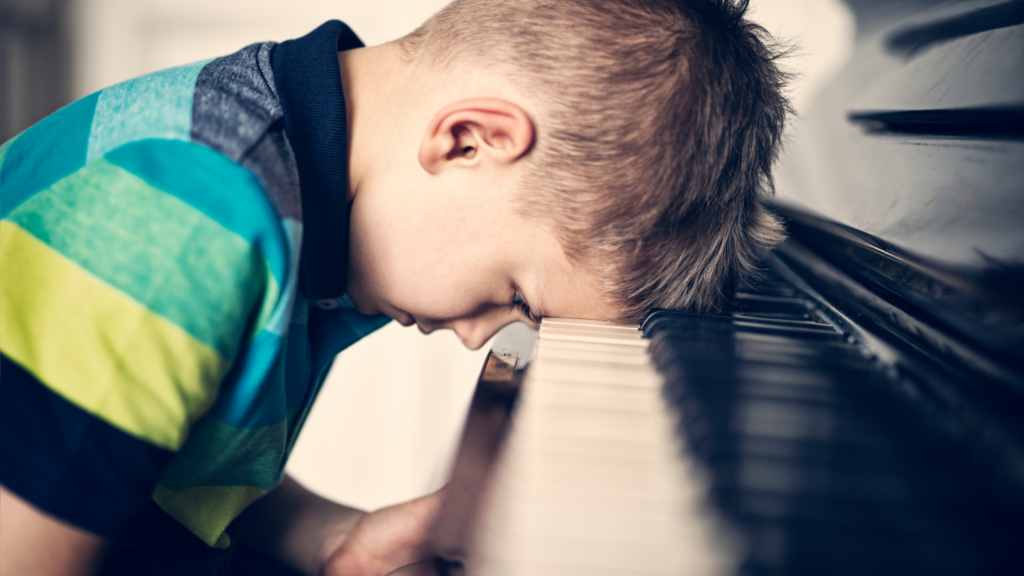 Child resting head on piano keys, showing that kids don’t like piano lessons at first
