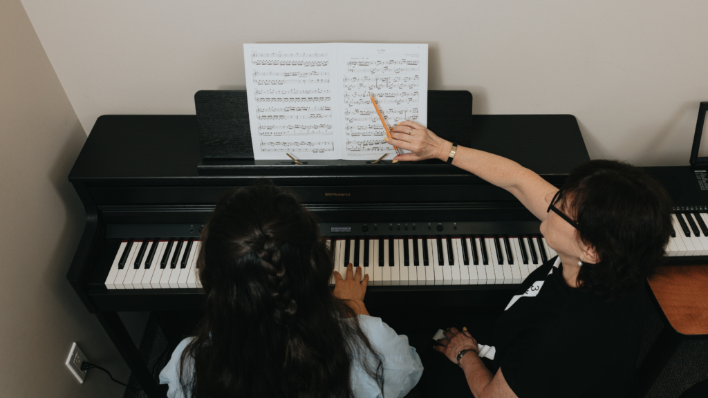 Young piano student learning alongside her teacher during a music lesson, focused on the keys while building confidence and musical skills in a supportive studio environment.
