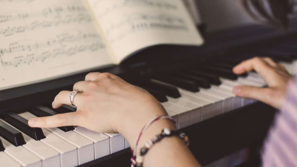 A young piano student's hands rest on the keys while reading sheet music during a lesson.